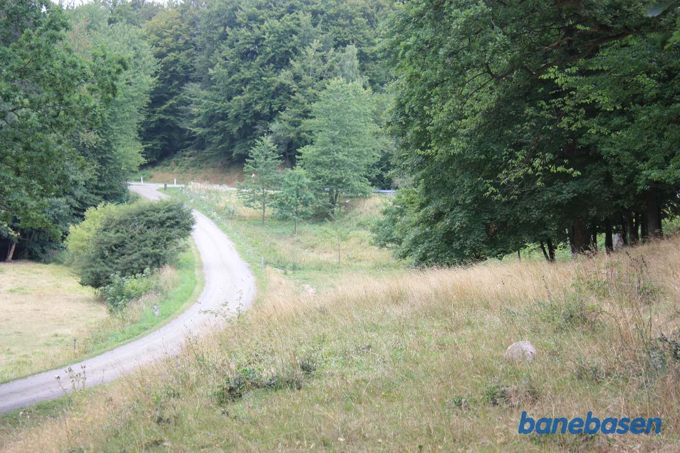 Vi står på den gamle banetracé og kigger mod Gudhjem. Banen slog en kurve mod venstre, men banedæmningen er her fjernet. Almindingsvejen ses længere fremme Vi står på den gamle banetracé og kigger mod Gudhjem. Banen slog en kurve mod venstre, men banedæmningen er her fjernet. Almindingsvejen ses længere fremme