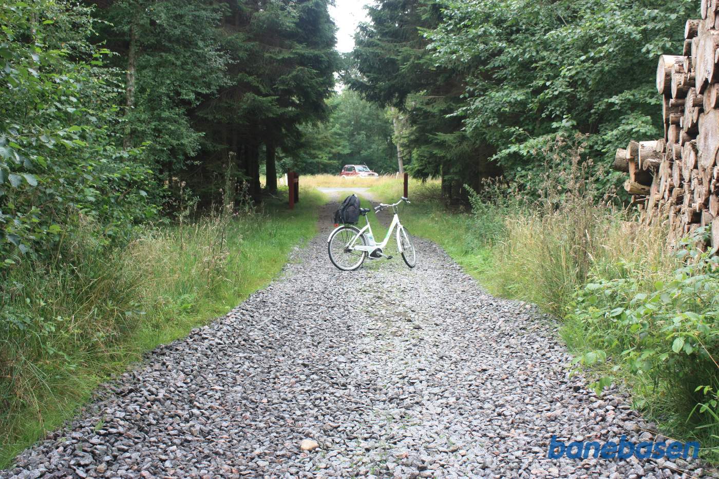 Vi står på en skovvej og cyklen markerer, hvor banen krydsede vejen. Gudhjem til venstre og Aakirkeby til højre Vi står på en skovvej og cyklen markerer, hvor banen krydsede vejen. Gudhjem til venstre og Aakirkeby til højre