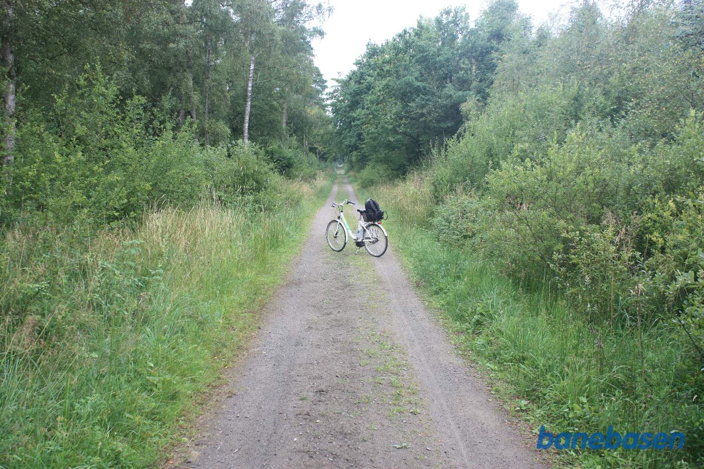 Vi står på en skovvej og cyklen markerer, hvor banen krydsede skovvejen, Aakirkeby til venstre og Gudhjem til højre Vi står på en skovvej og cyklen markerer, hvor banen krydsede skovvejen, Aakirkeby til venstre og Gudhjem til højre
