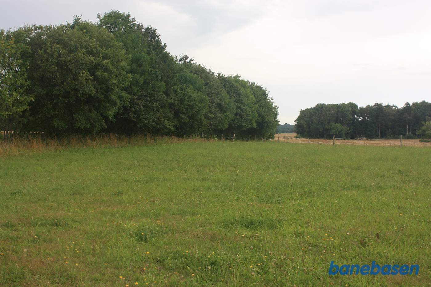 Vi står på Savmøllevej og kigger mod Gudhjem. Banen gik inde mellem rækken af træer til venstre i en dyb udgravning, fortsatte over det åbne markstykke og venstre om træerne i skoven overfor. Man kan se i markskellet henover marken, hvor banen gik Vi står på Savmøllevej og kigger mod Gudhjem. Banen gik inde mellem rækken af træer til venstre i en dyb udgravning, fortsatte over det åbne markstykke og venstre om træerne i skoven overfor. Man kan se i markskellet henover marken, hvor banen gik