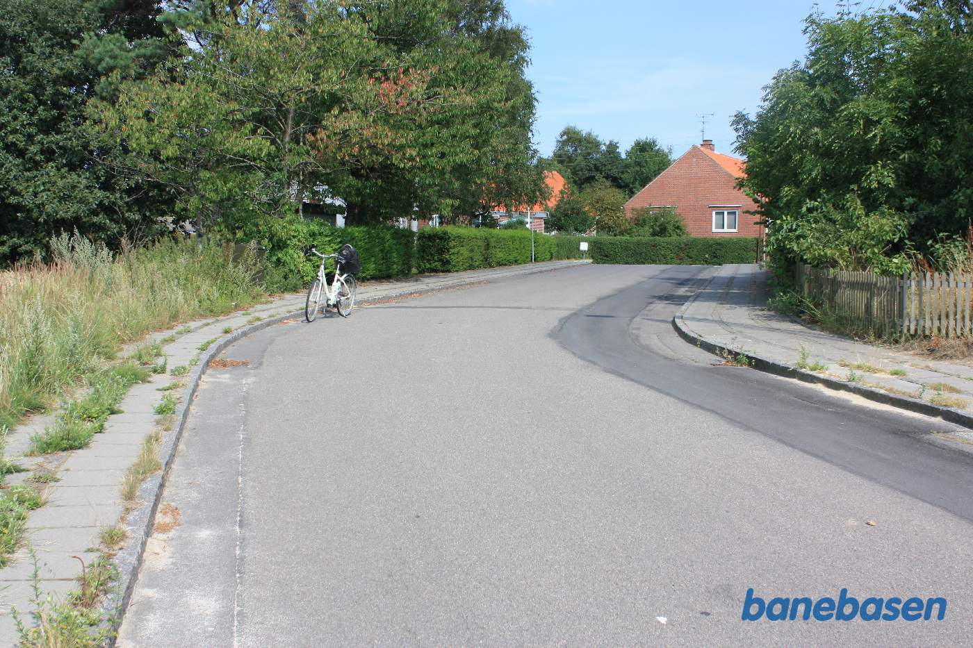 Vi står på Rosenørns Allé. Cyklen markerer, hvor banen i sin tid gik længe før villakvarteret her blev bygget. Gudhjem til venstre og Aakirkeby til højre