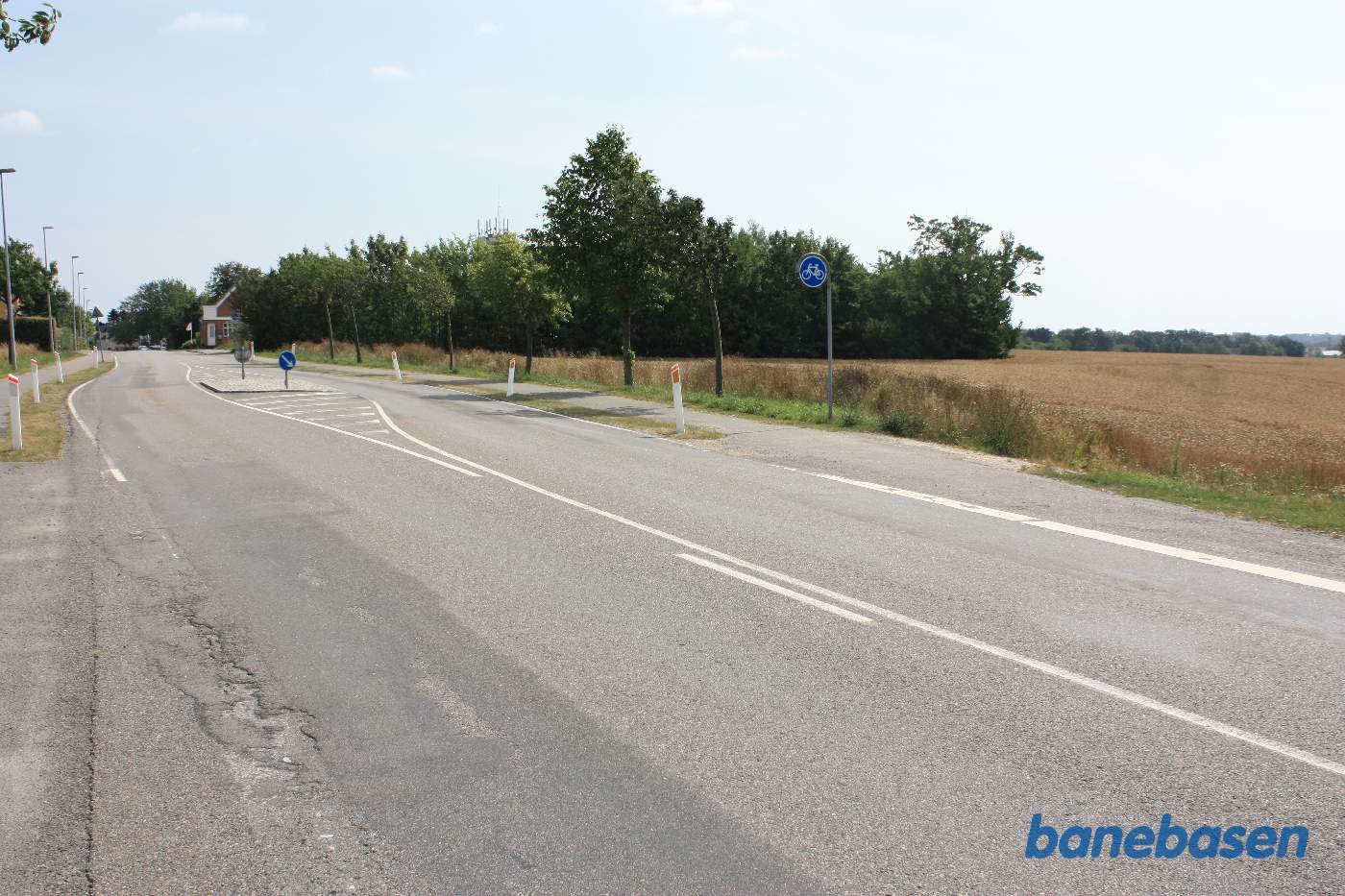 Vi står på Godthåbsvej, hvor banen krydsede vejen. På grund af den spidse vinkel, slog vejen et zigzag sving, så vejen kom vinkelret på banen. Stationen ligger lige bag træerne midt i billedet. Vi kigger mod Aakirkeby Vi står på Godthåbsvej, hvor banen krydsede vejen. På grund af den spidse vinkel, slog vejen et zigzag sving, så vejen kom vinkelret på banen. Stationen ligger lige bag træerne midt i billedet. Vi kigger mod Aakirkeby
