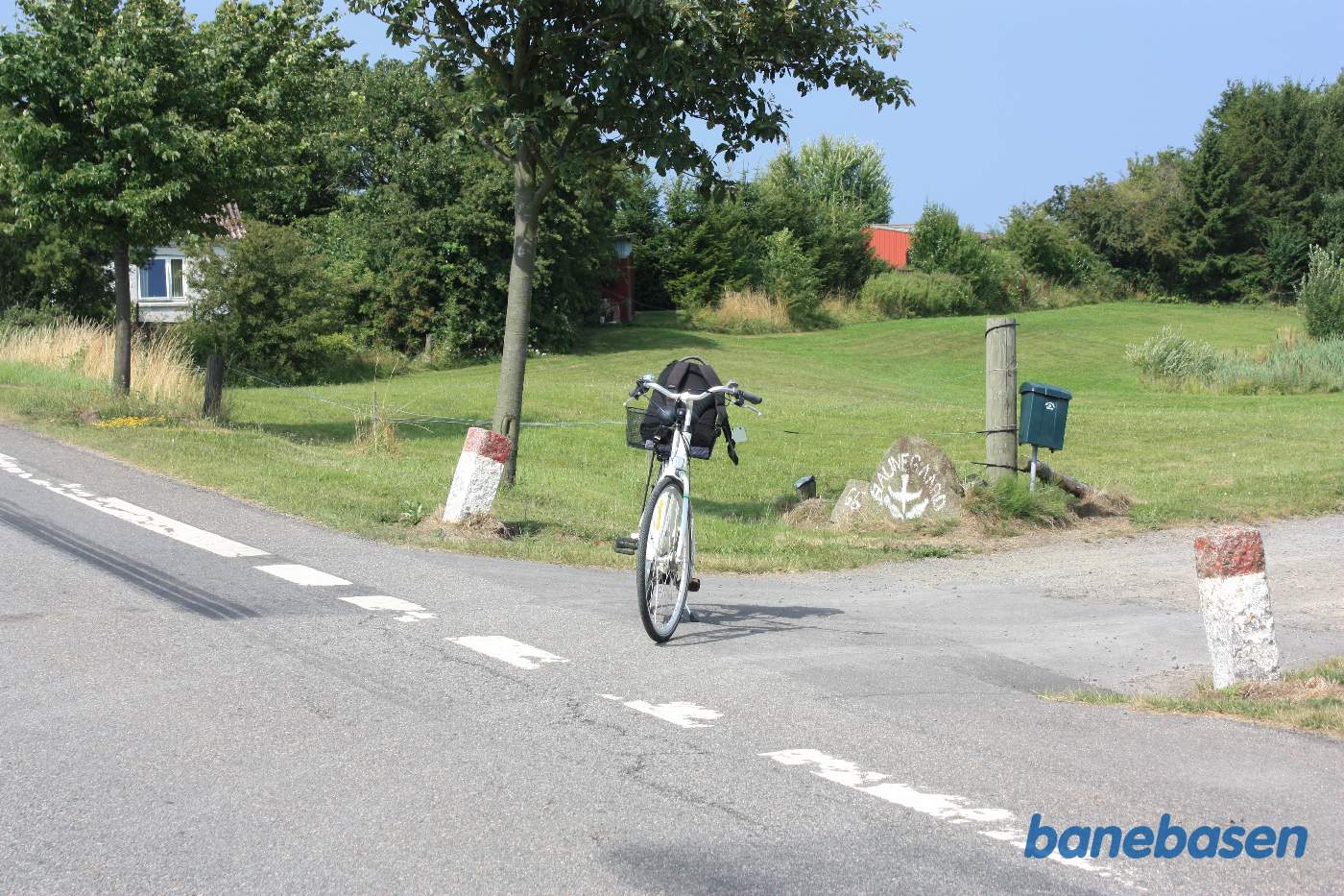 Vi står på Godthåbsvej, hvor banen krydsede vejen. Man kan stadig fornemme resterne af banedæmningen lige bag cyklen. Vi kigger mod Gudhjem