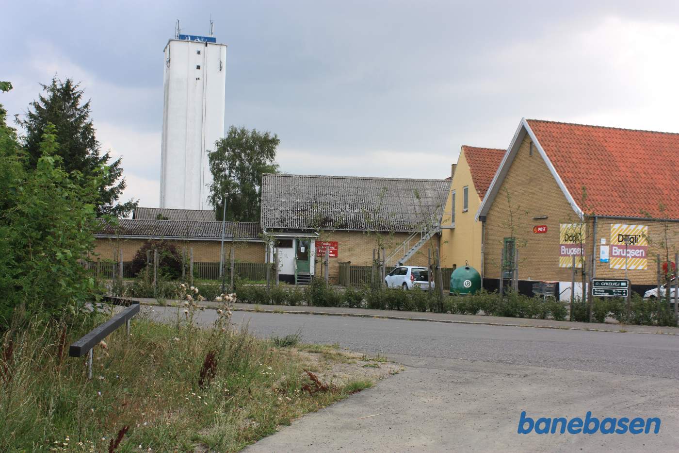 Vi kigger på Gamlevældevej, hvor banen krydsede vejen og gik ind gennem den gule murstensbygning med gråt eternit tag Vi kigger på Gamlevældevej, hvor banen krydsede vejen og gik ind gennem den gule murstensbygning med gråt eternit tag