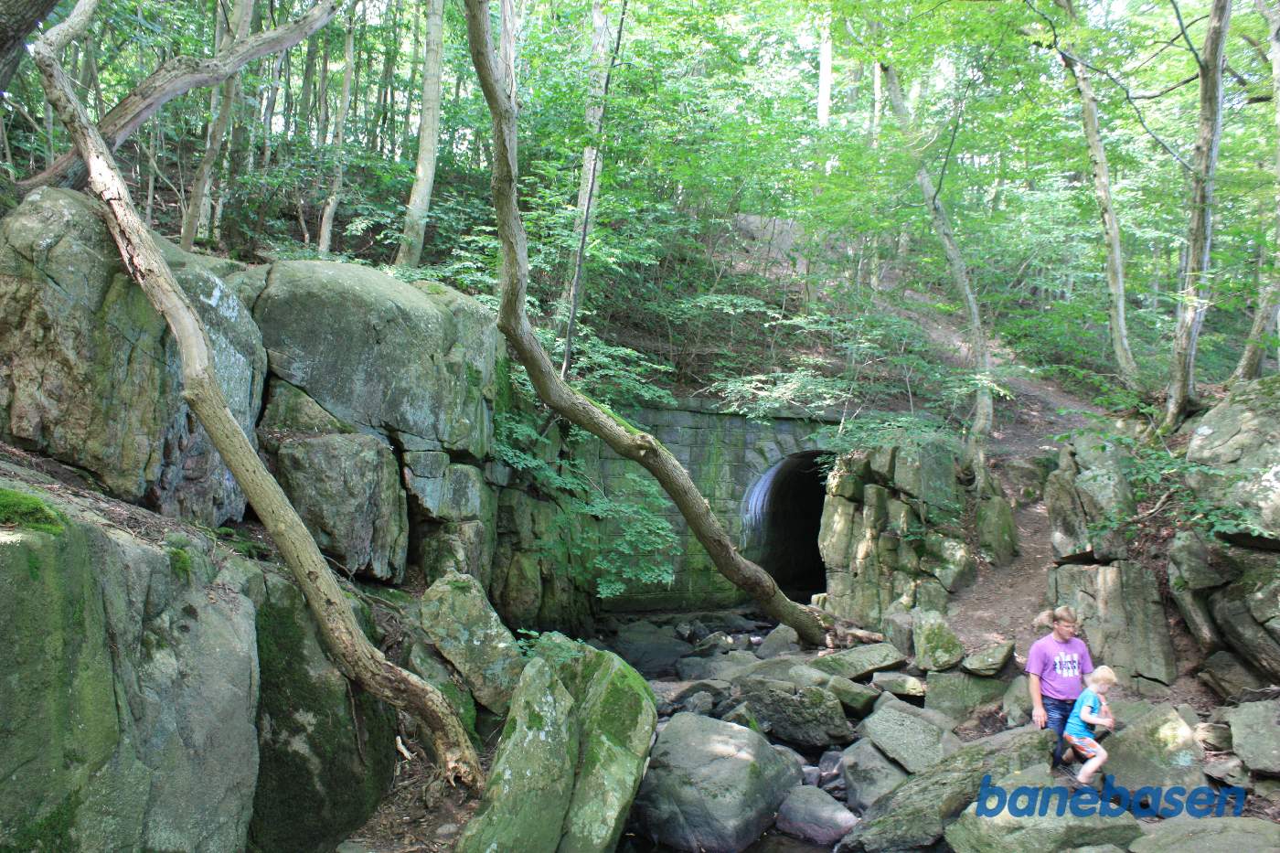 Vi står ved Kobbeå og kigger på den flotte stenkanal for åen samt op på den meget høje banedæmning. Aakirkeby til venstre og Gudhjem til højre
