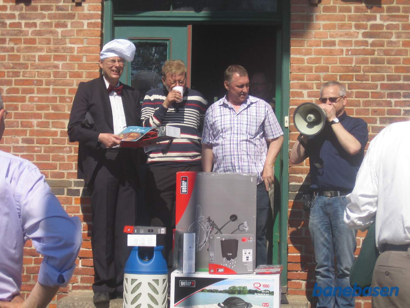 På trappen op til stationen, overrækkes de to fødselarer gaverne fra Jernbaneklubben, mens medlemmerne ser på På trappen op til stationen, overrækkes de to fødselarer gaverne fra Jernbaneklubben, mens medlemmerne ser på
