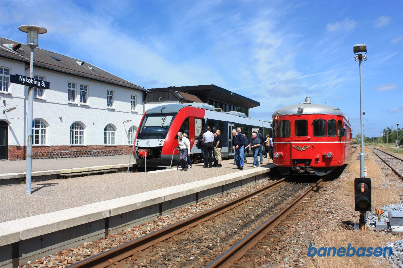 Udflugtstoget er kommet til Nykøbing Sj. Hvor gæsterne myldre ud på perronen, et Lokaltog i spor 1 Udflugtstoget er kommet til Nykøbing Sj. Hvor gæsterne myldre ud på perronen, et Lokaltog i spor 1