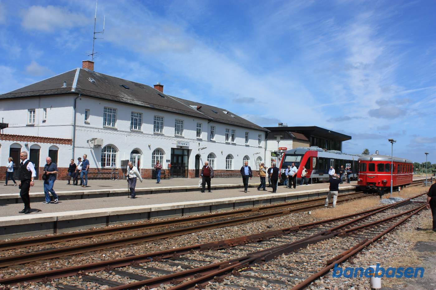Udflugtstoget er kommet til Nykøbing Sj. Hvor gæsterne myldre ud på perronen og spredes over hele stationsområdet, et Lokaltog i spor 1 Udflugtstoget er kommet til Nykøbing Sj. Hvor gæsterne myldre ud på perronen og spredes over hele stationsområdet, et Lokaltog i spor 1