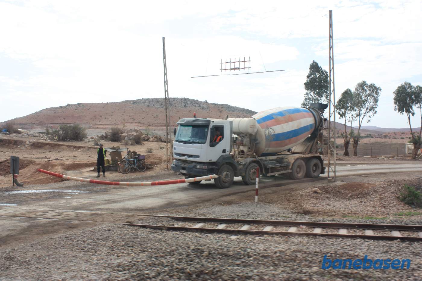 En cementblander holder for bommen mens toget suser over vejen