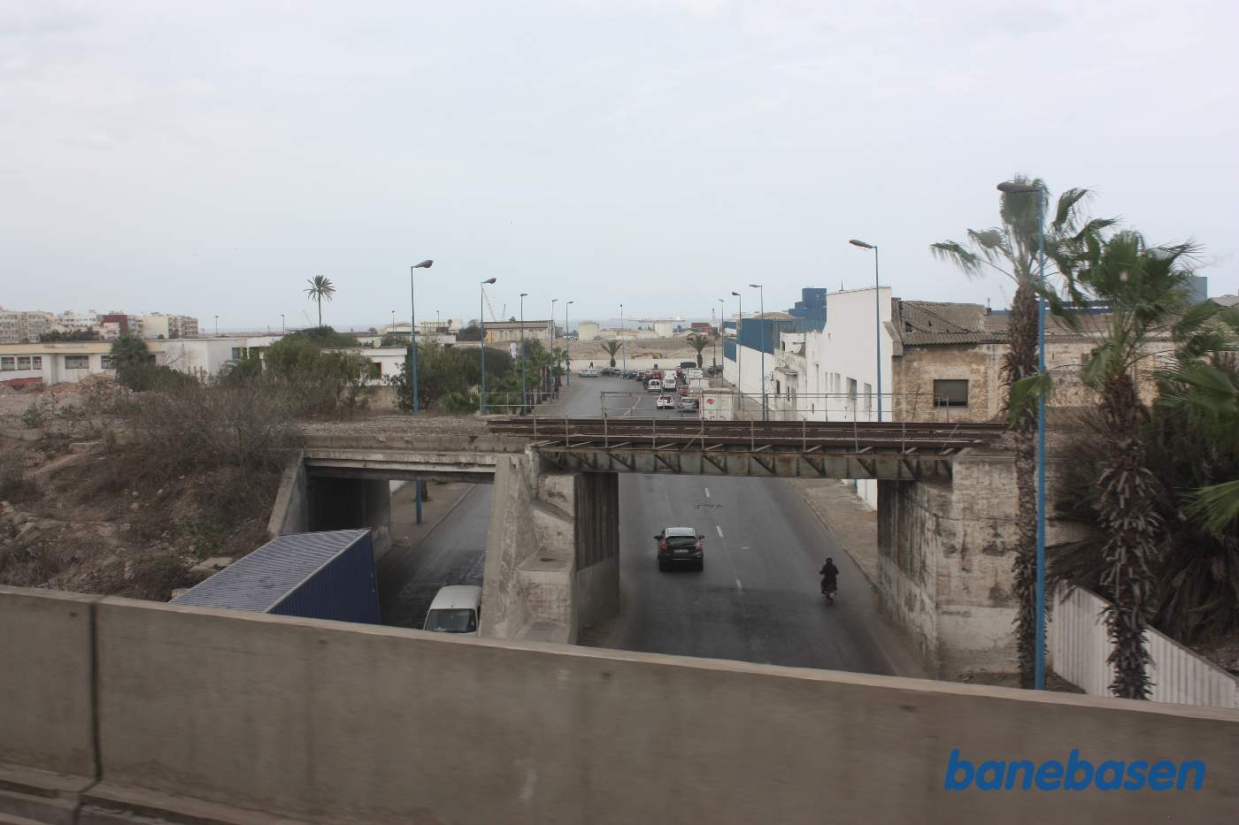 Jernbanebro, hvor skinnerne er fjernet, kysten med stort fragtskib ses ude på havet