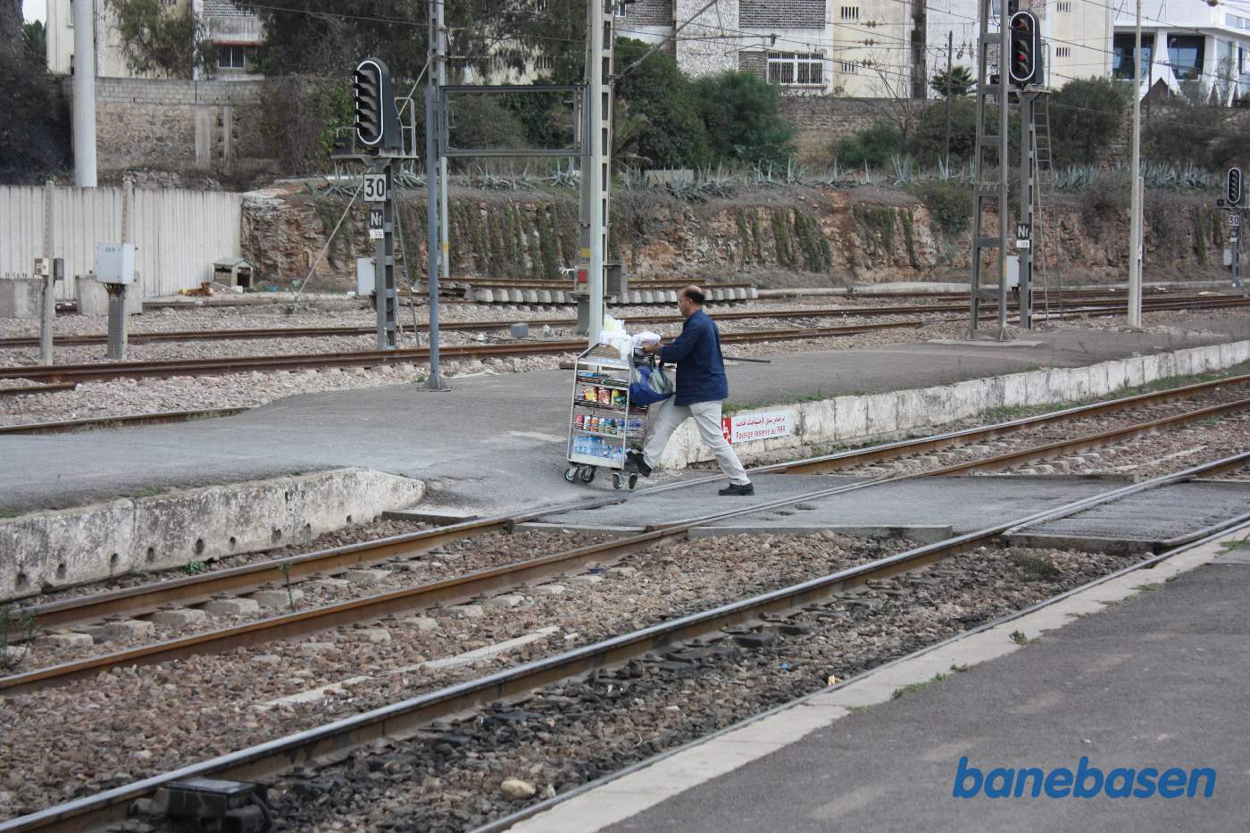 En perronsælger med lille vogn krydser over sporene med sin vogn