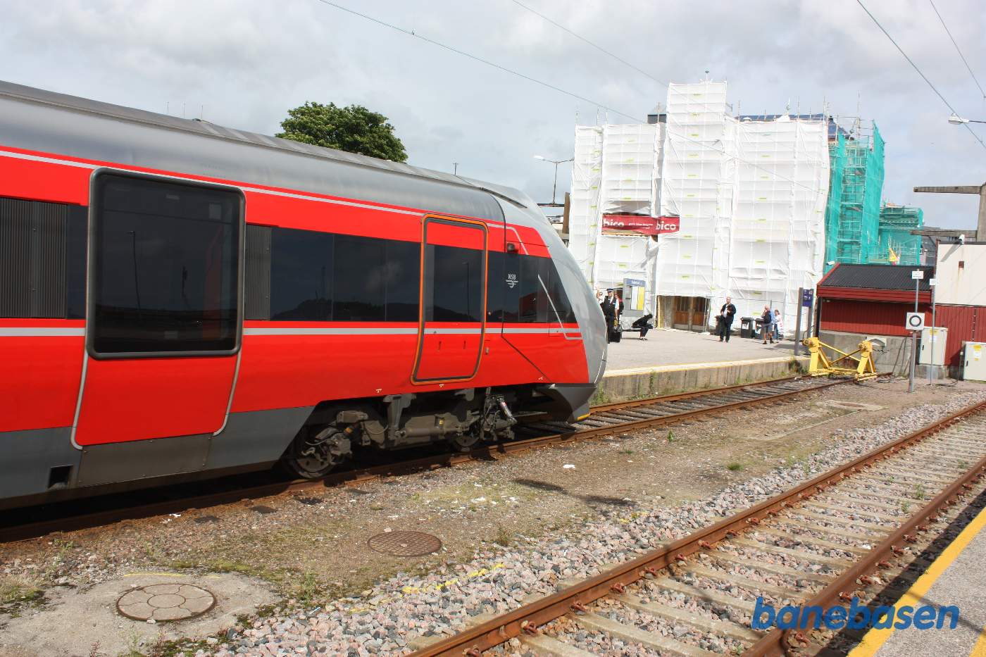 Elektrisk togsæt på vej ind på stationen. Stationsbygningen ses pakket ind i presenninger
