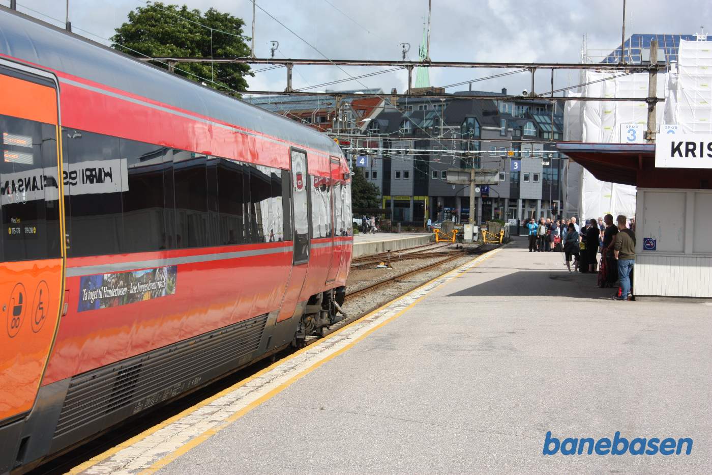 Elektrisk togsæt på vej ind på stationen i spor 3. Rejseholdet står på perronen og kigger på