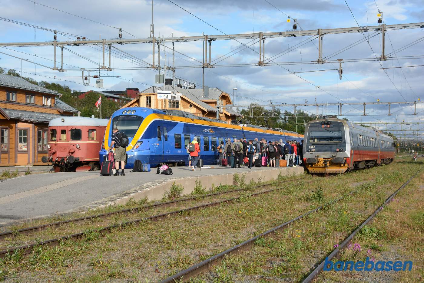 3 persontog ved perron. Passagerer, der skal videre mod Trondheim, står på midterperronen og venter på toget fra Trondheim er tømt, så de kan komme ind i toget, mens rejsende fra Trondheim skal over i det blå tog mod Östersund