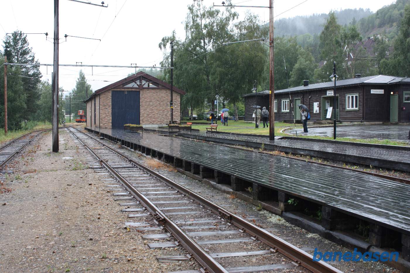 Et vue ud over træperronen med remisen af sten midt i billedet. Gæsterne går i regnvejret over til selve museet
