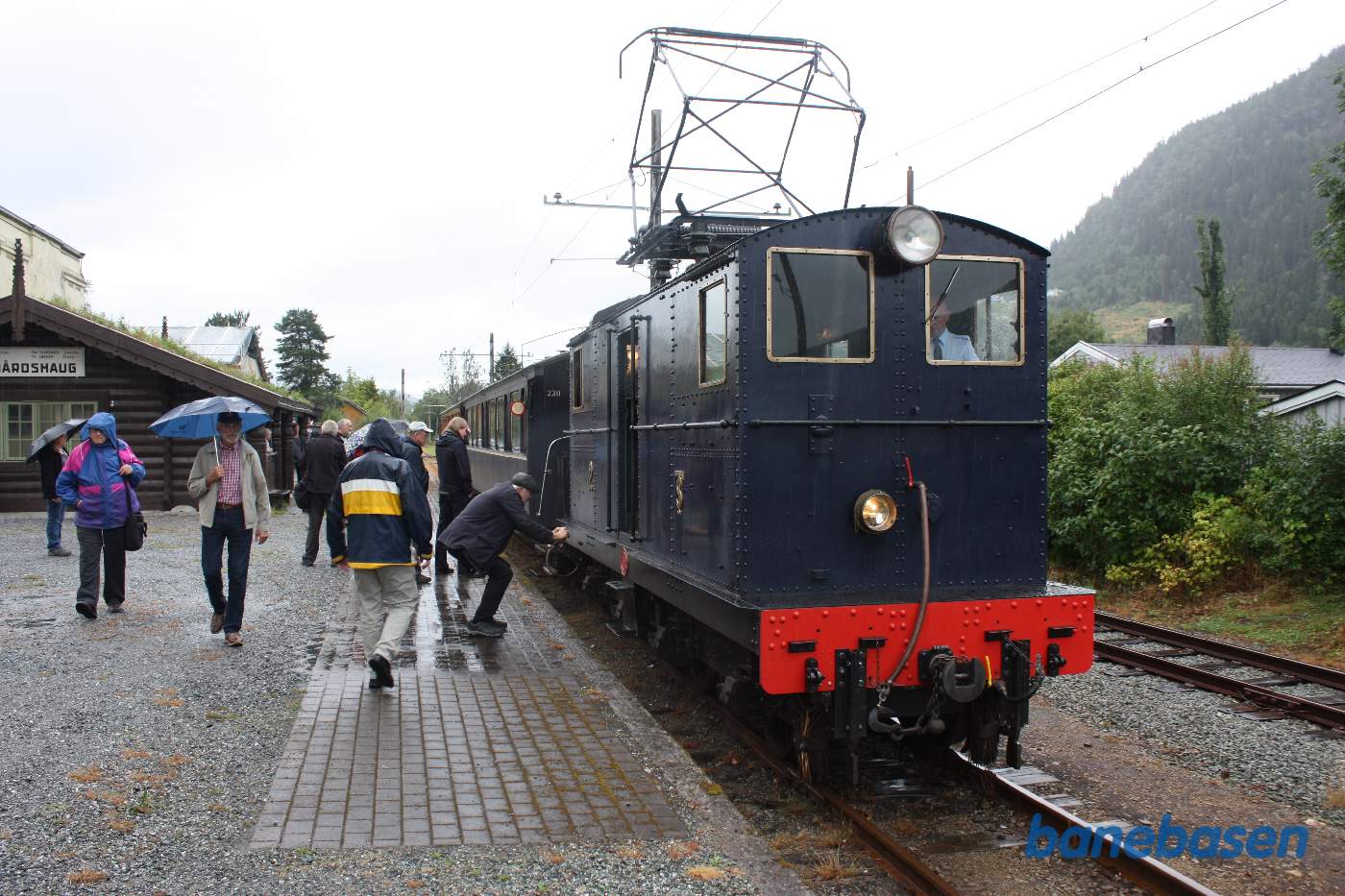Toget holder ved perron med den lille stationsbygning, opført af træstammer, til venstre