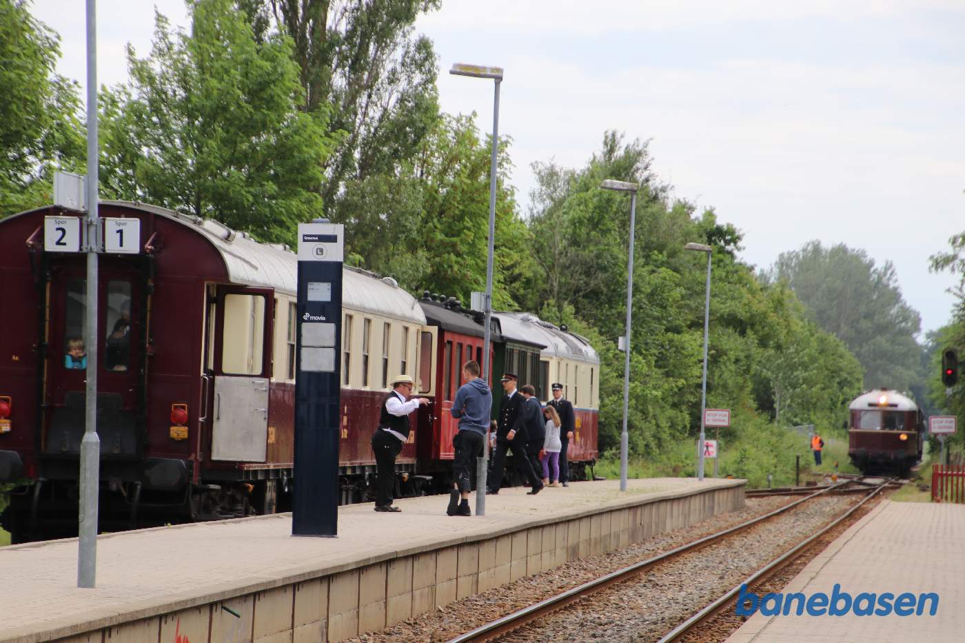 Det ene persontog holder i spor 2 med HFHJ M 8 mens det andet persontog med GDS L 1 er på vej ind på stationen fra Mårum