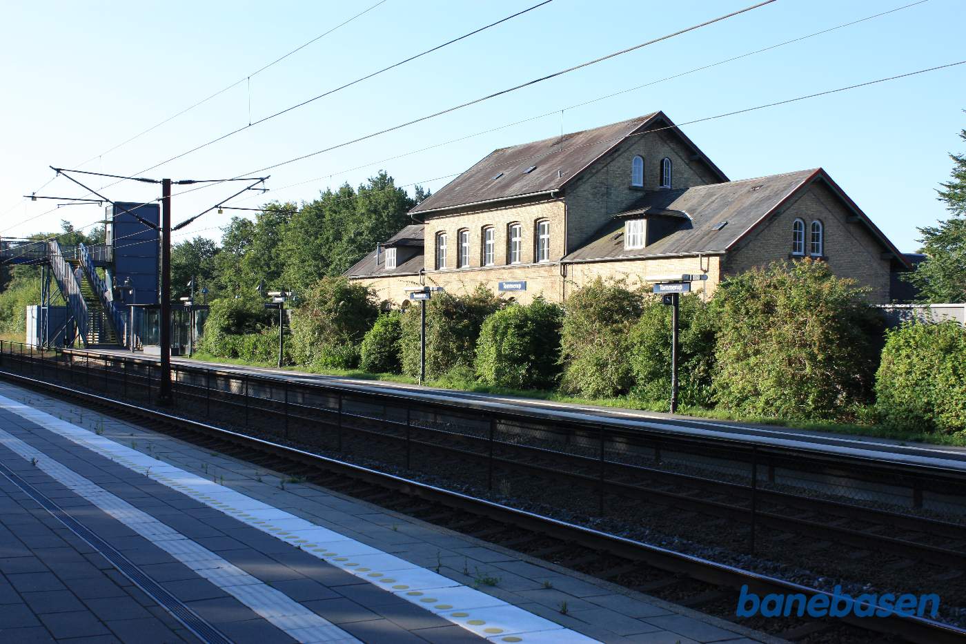 Tommerup stationsbygning, gemt inde bag en række træer, set fra banen