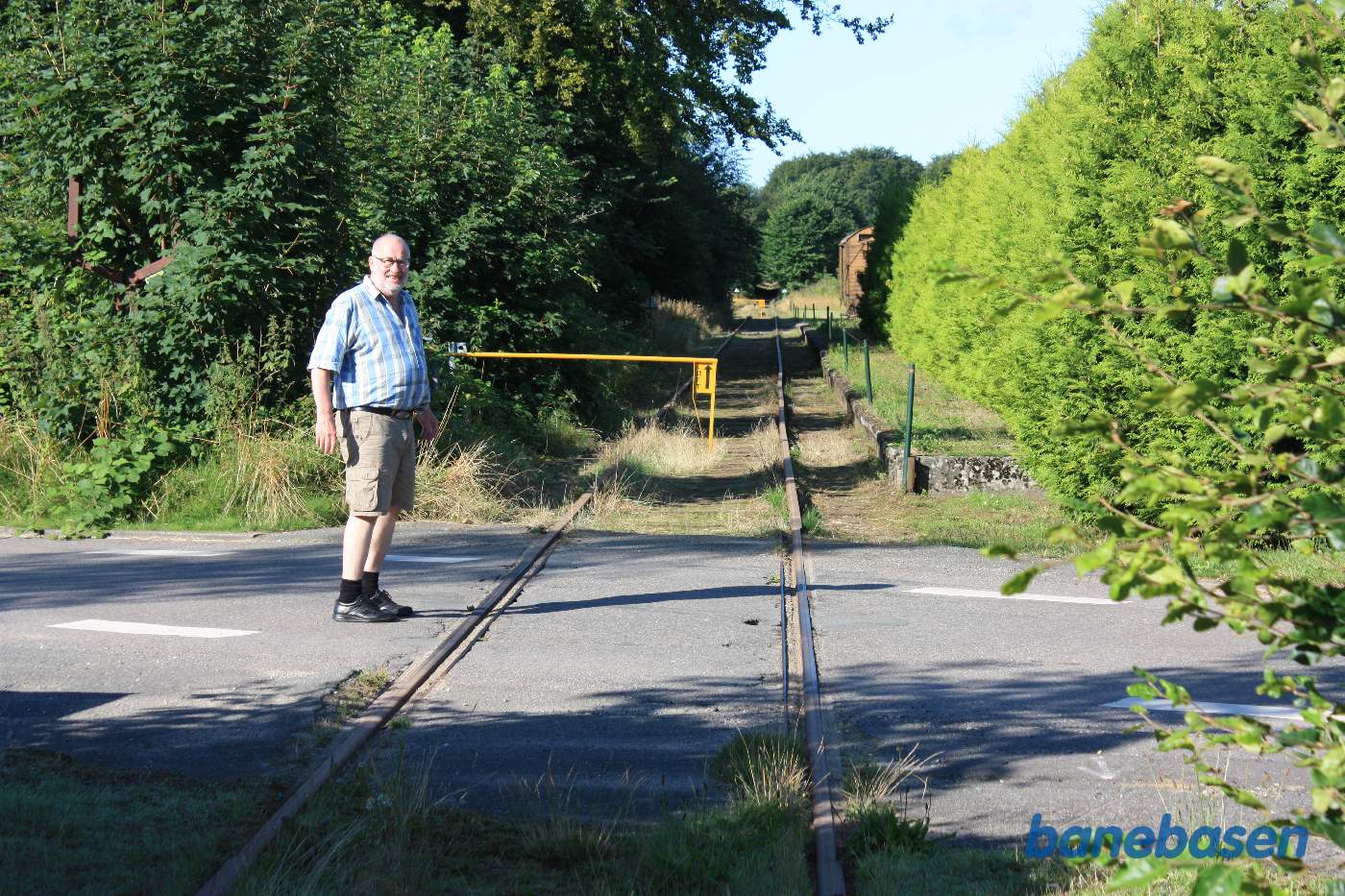 Vi er nået til Nårup, og skal krydse Skovsbovej, perronen til højre. Inde til venstre, helt overgroet, ses de rustne rester af vejbommen med wiretræk inde fra stationen
