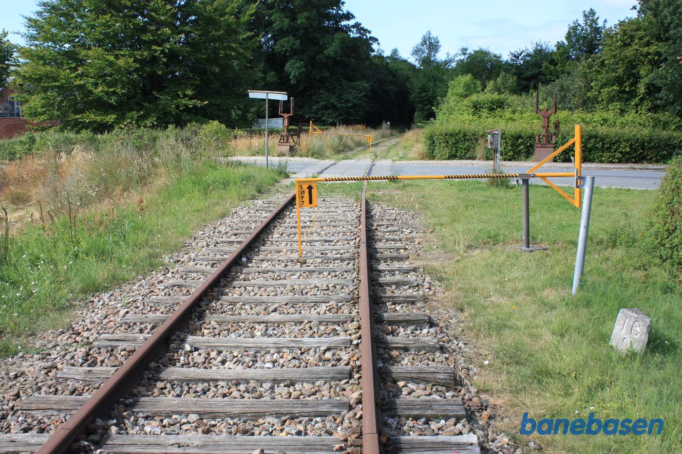 Vi er stoppet op lige udenfor Flemløse for at krydse Langgade. Stationen ligger til højre inde bag træerne. Bemærk de rustne rester fra vejbommene med wiretræk inde fra stationen