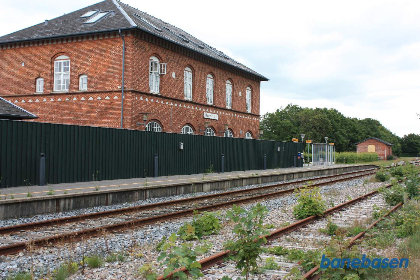 Stationsbygningen, gemt inde bag et højt plankeværk, set fra perronen