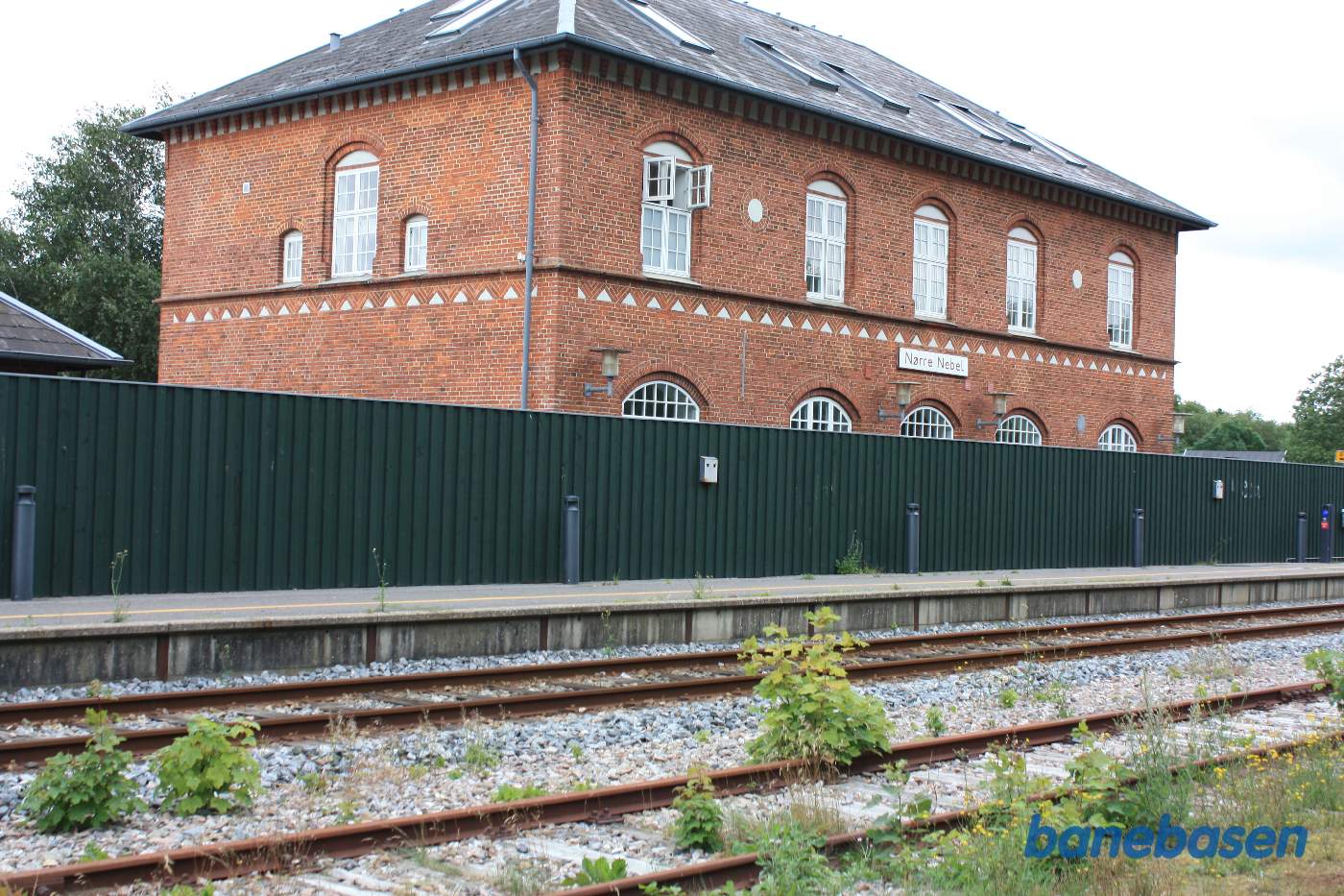 Stationsbygningen, gemt inde bag et højt plankeværk, set fra perronen