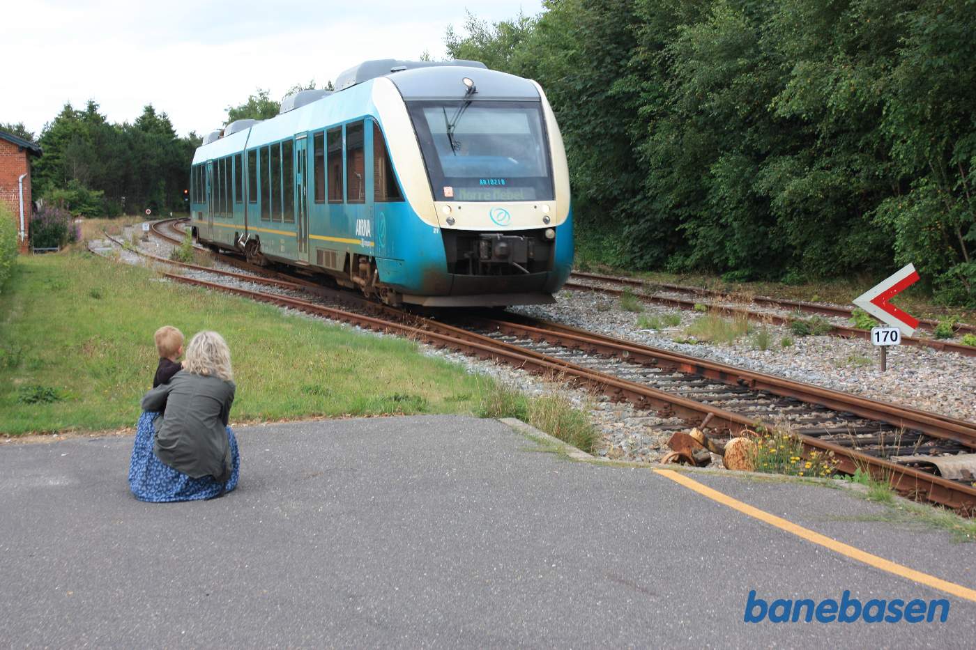Et Arriva togsæt på vej ind på stationen, mor med søn kigger på