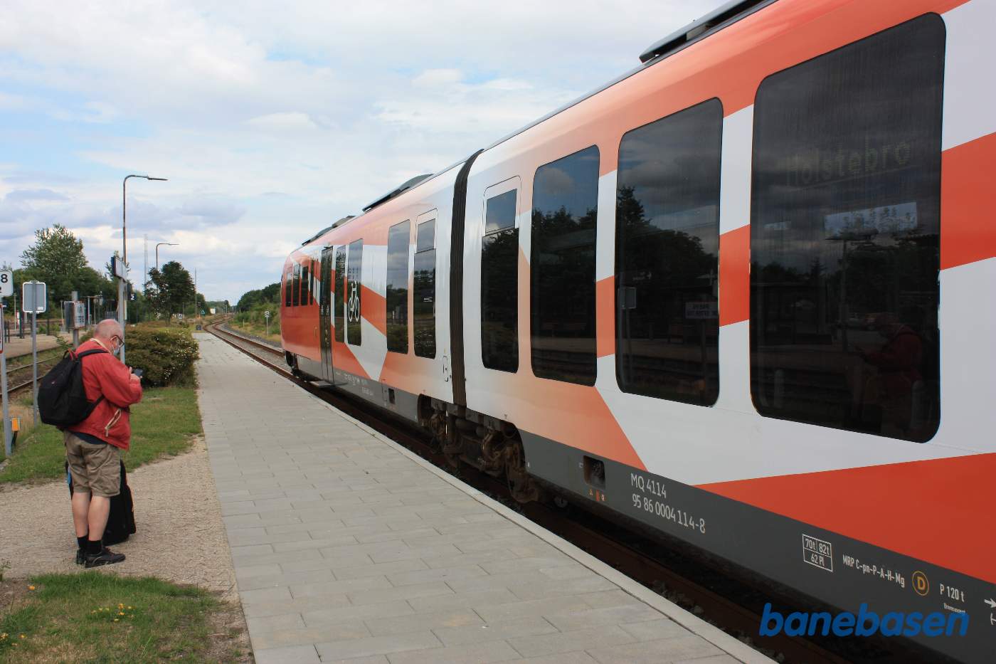 Et lokaltog ved perron mens en passager tjekker sin mobiltelefon