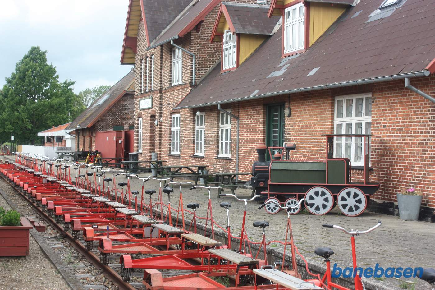 En række skinnecykler holder klar i perronsporet, stationsbygningen i baggrunden En række skinnecykler holder klar i perronsporet, stationsbygningen i baggrunden