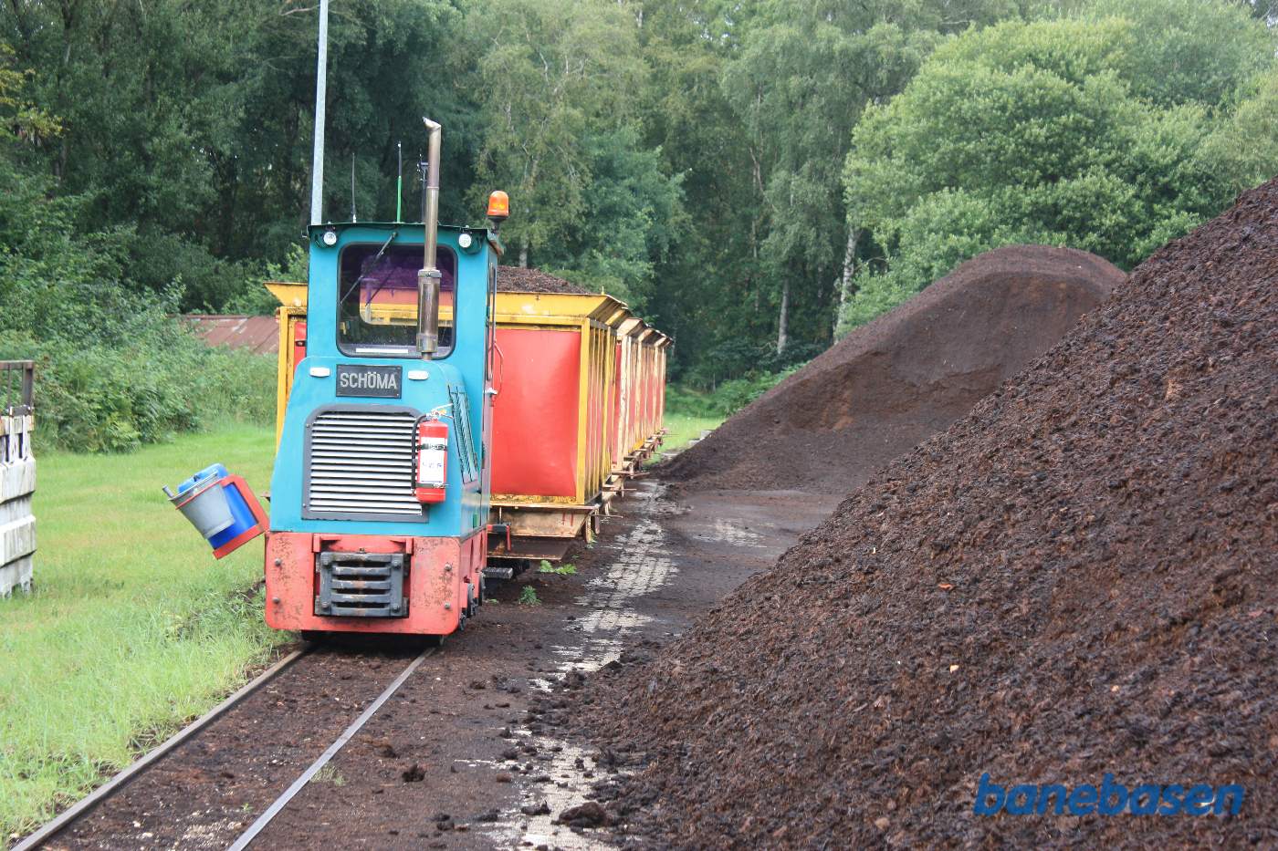 Det lille diesellokomotiv foran vogne til løs mosejord. En bunke mosejord ses til højre