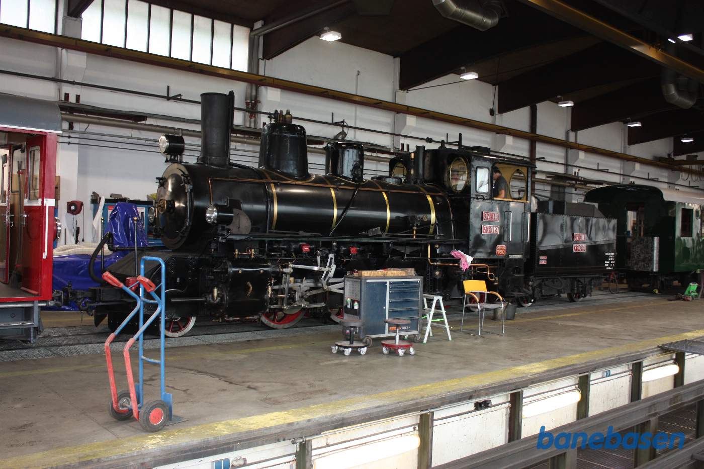 Inde i værkstedet står bl.a. et damplokomotiv, en håndværker arbejder oppe i førerhuset
