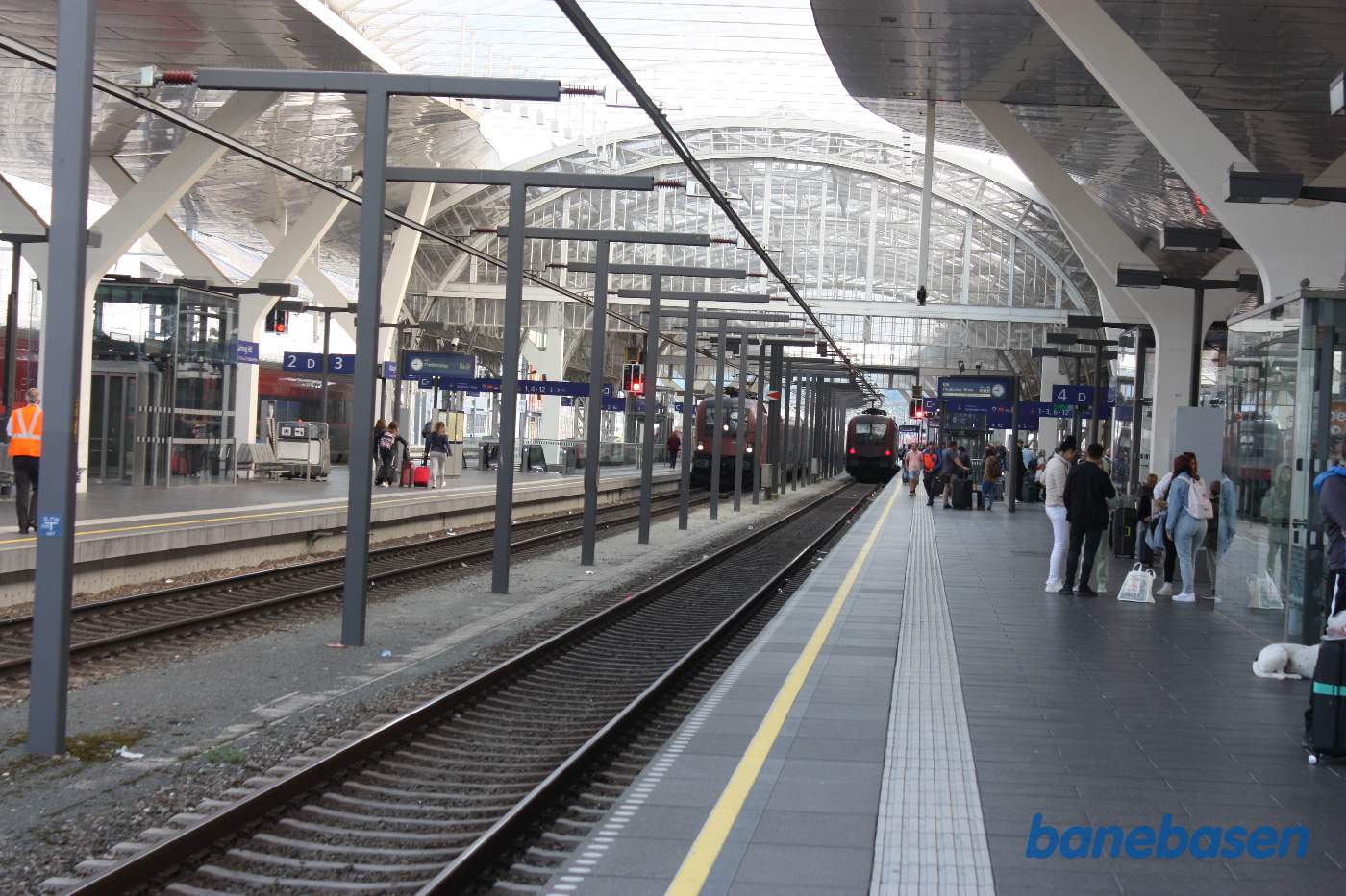 Et vue ud over perronerne med tog og passagerer samt den gamle hal