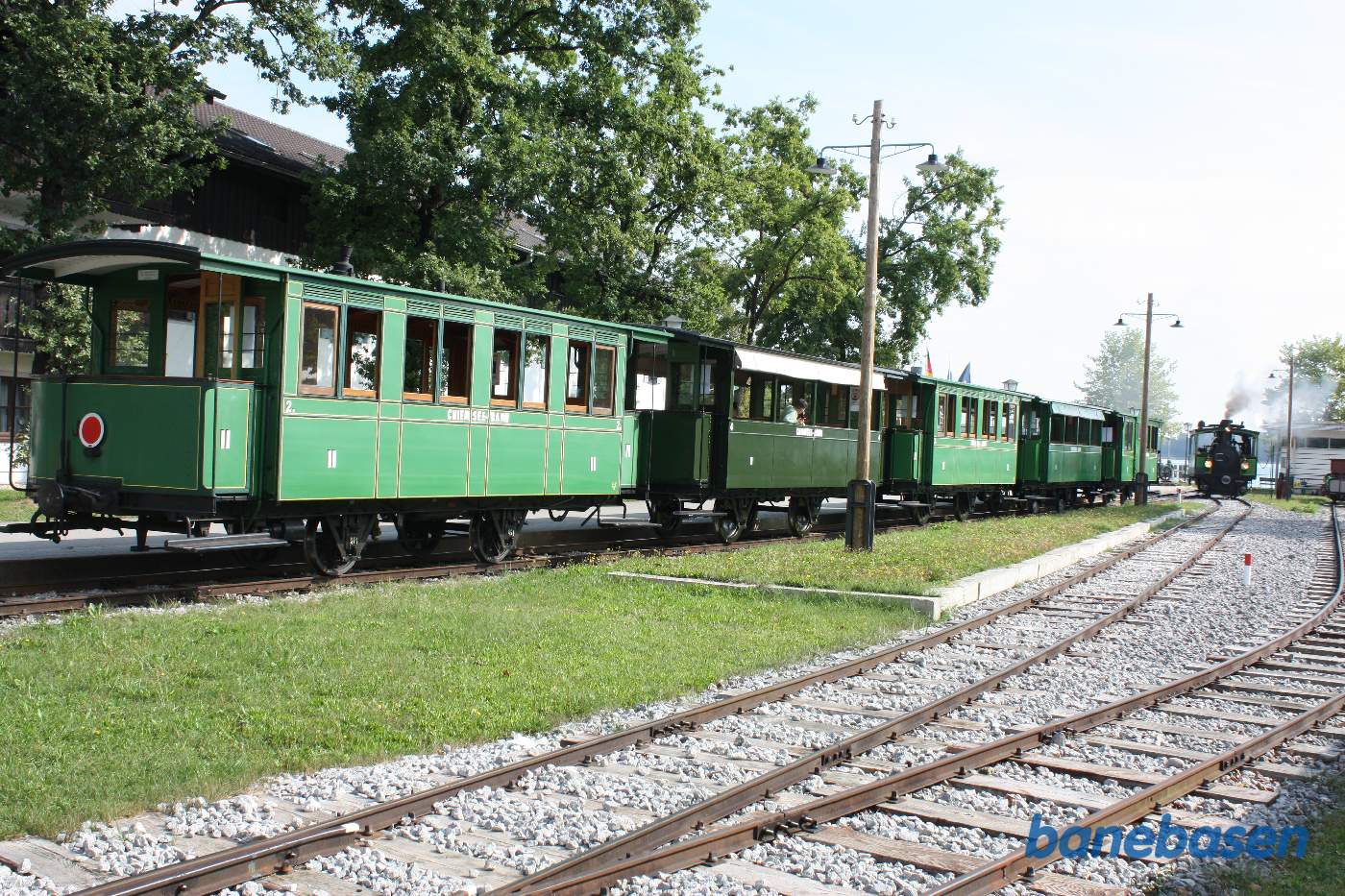 Personvognene holder ved perron mens damplokomotivet løber om