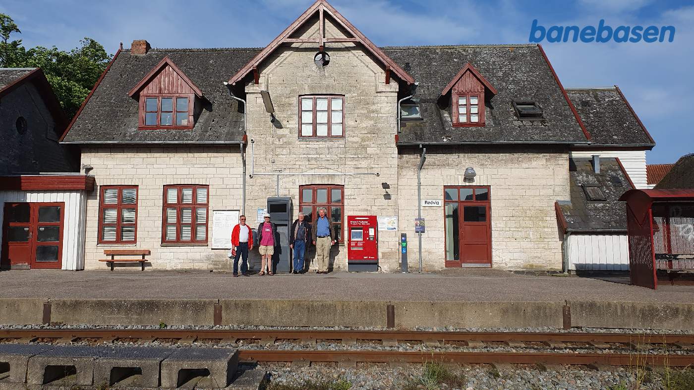 Stationsbygningen set i eftermiddagens bløde lys med 4 rejsende på perronen Stationsbygningen set i eftermiddagens bløde lys med 4 rejsende på perronen