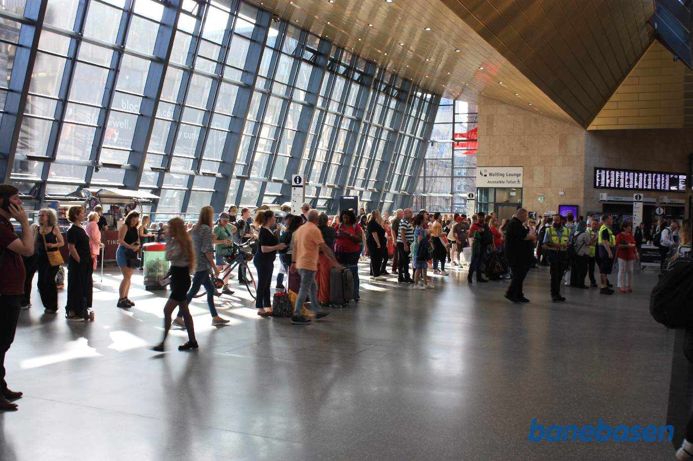 Et vue ud over området for enden af sporene med mange travle personer. Udenfor de store glasruder ligger W George Street