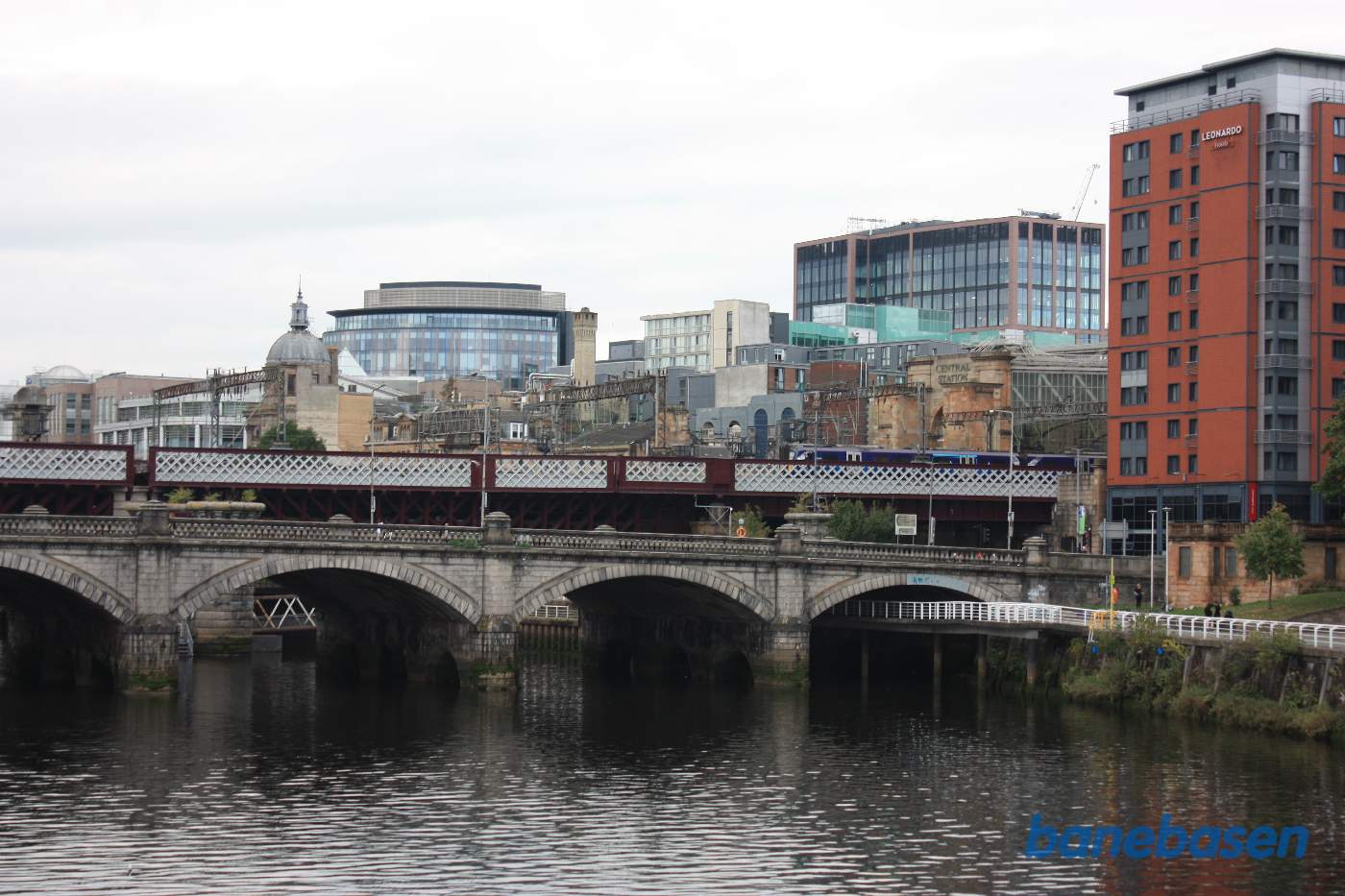 Jernbanen går på en meget bred bro over floden Clyde, broen Glasgow Bridge ses i forgrunden. Centralstationen ses inde til højre