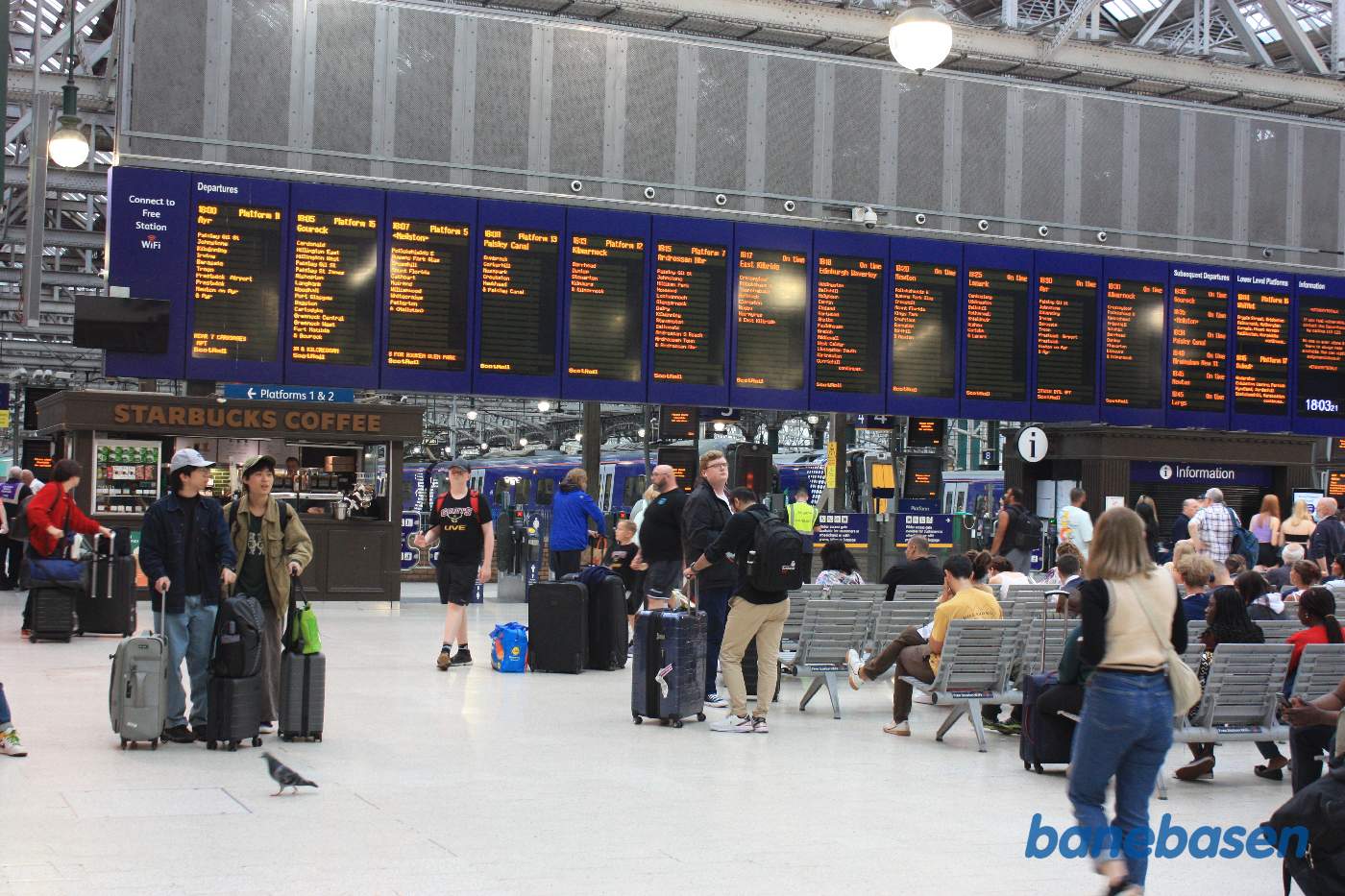 Den store afgangstavle inde i stationens afgangshal med mange ventende passagerer