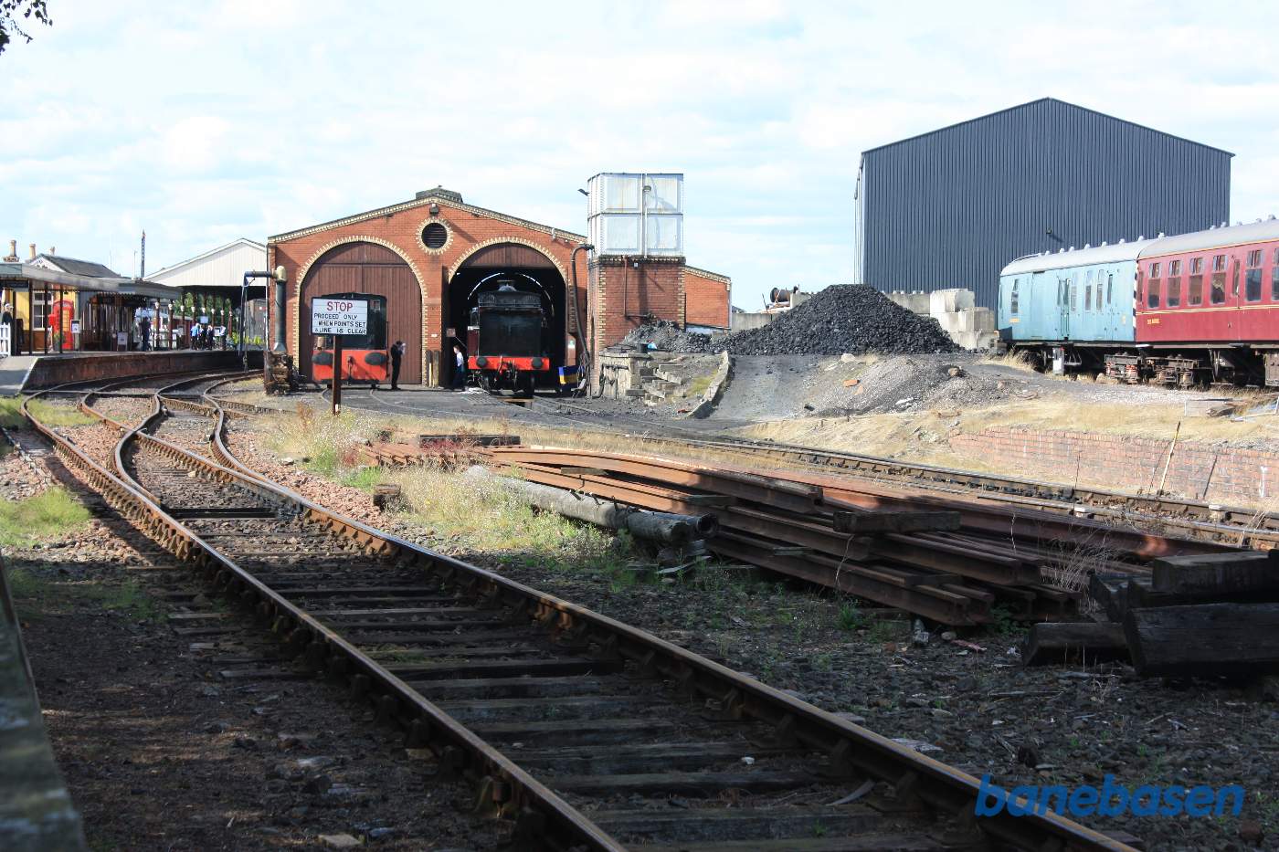 Et flot damplokomotiv står foran porten til remisen, perronsporet og stationsbygningen til venstre i billedet