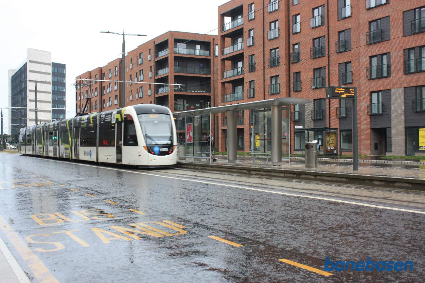 Sporvogn til lufthavnen ses her i regnvejr nær havnen med stoppested i baggrunden