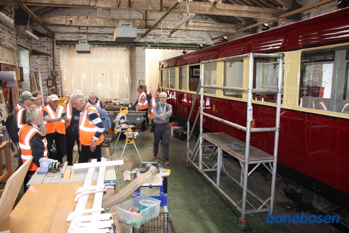 Et vue ud over det næste vognværksted med dele på bordene. En rød-beige salonvogn til højre